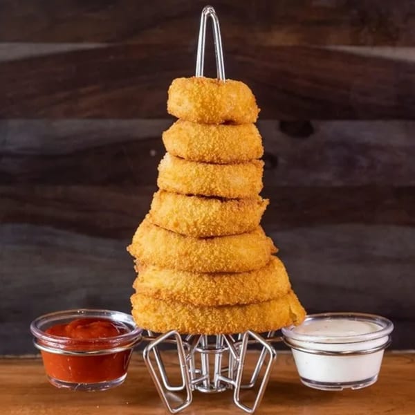 A tall stack of golden-brown onion rings on a metal stand, with ketchup and ranch dipping sauces.