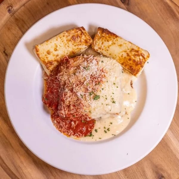 Chicken parmesan with red and white sauce, topped with cheese and parsley, served with garlic bread.