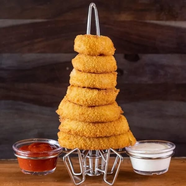 A tall stack of golden-brown onion rings on a metal stand, with ketchup and ranch dipping sauces.