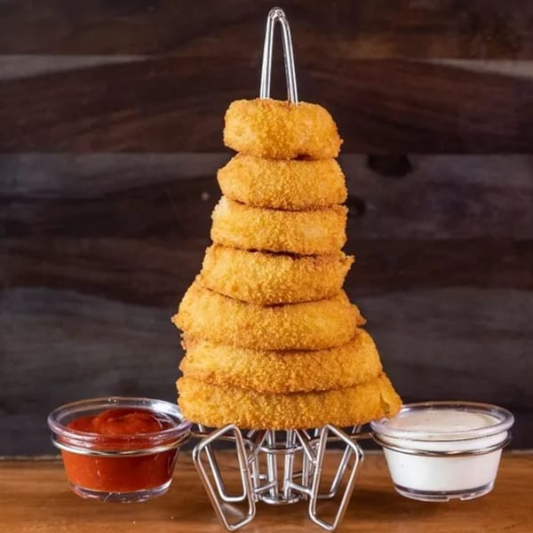 A tall stack of golden-brown onion rings on a metal holder, with ketchup and ranch dipping sauces.