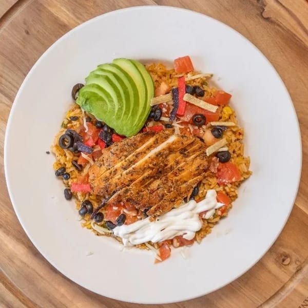 Chicken and rice bowl with avocado, black beans, tomatoes, and sour cream on a white plate.