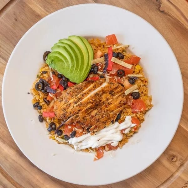 Chicken and rice bowl with avocado, black beans, tomatoes, and sour cream on a white plate.