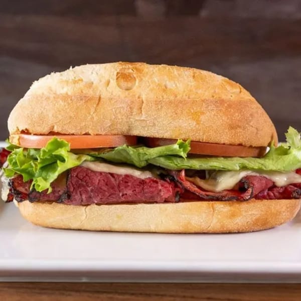 A Frends Brewhouse pastrami sandwich with melted cheese, lettuce, and tomato on a white plate.