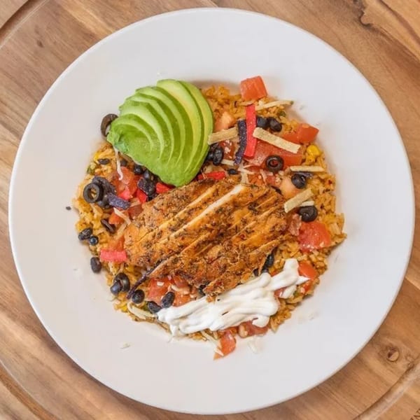 Chicken and rice bowl with avocado, black olives, tomatoes, and sour cream on a white plate.