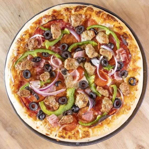Overhead view of a Frends Brewhouse pizza with pepperoni, sausage, ham, green peppers, black olives, and red onions.