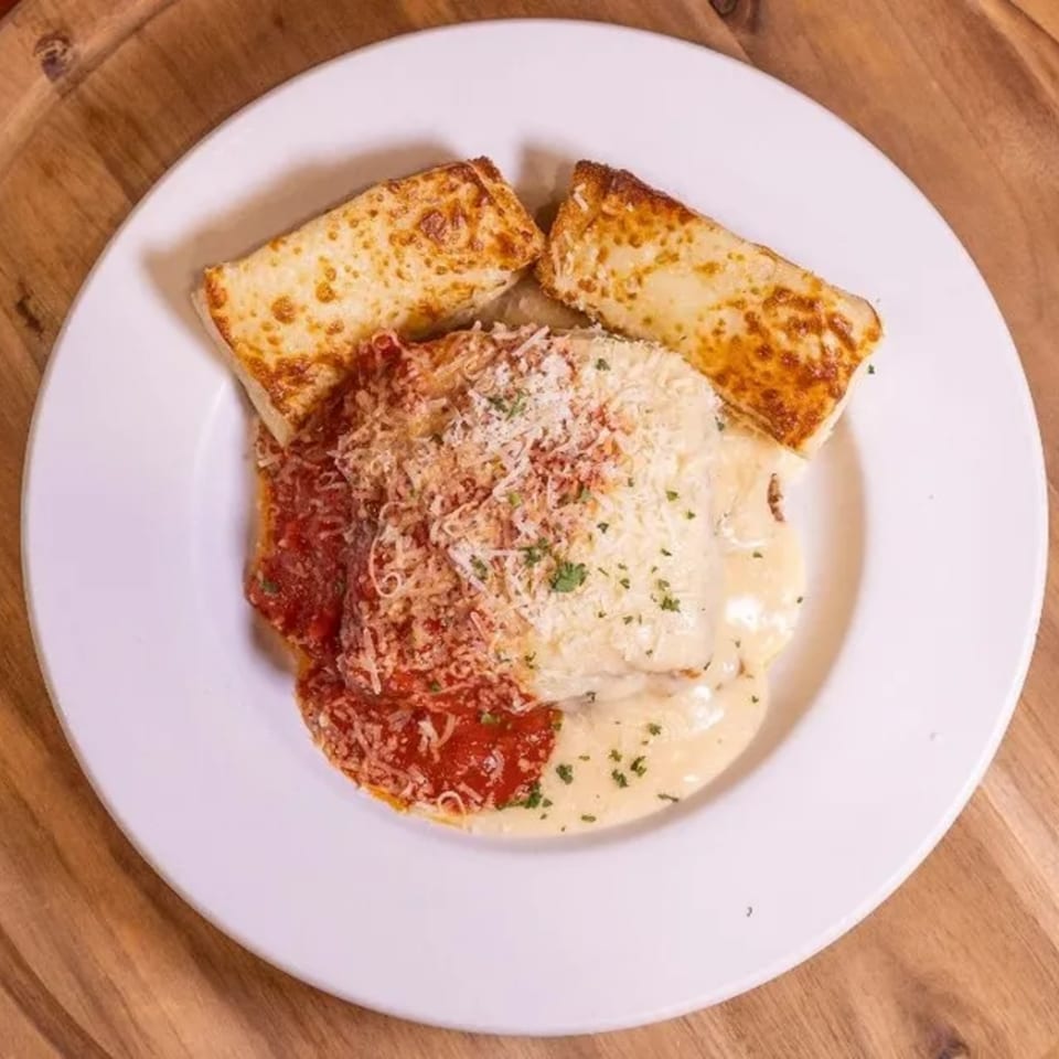 A Frends Brewhouse lasagna dish with red and white sauce, topped with cheese and two garlic bread slices.