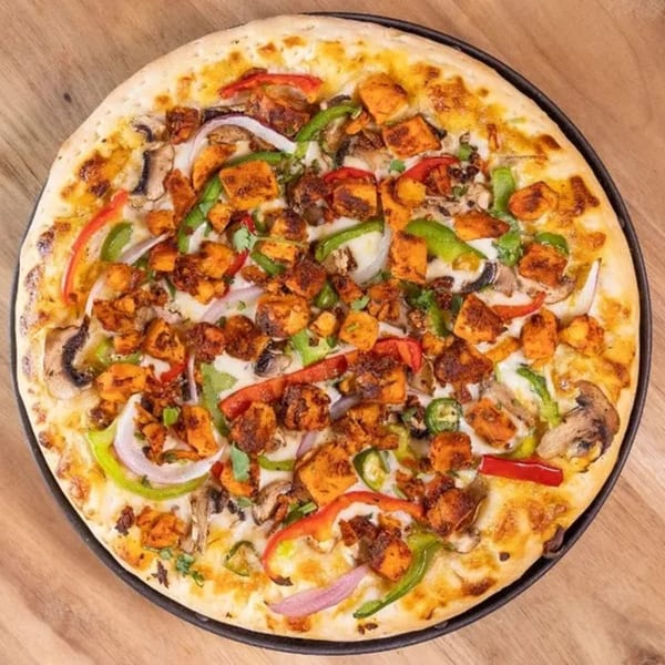 A Frends Brewhouse pizza with chicken, mushrooms, onions, and bell peppers on a wooden table.