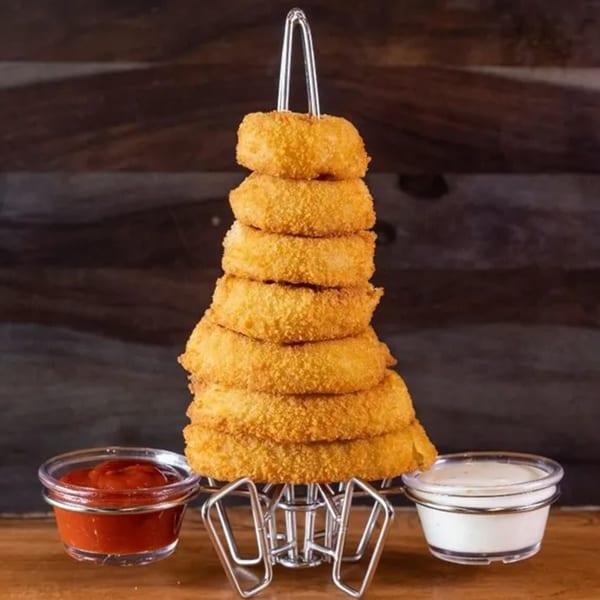 Tall stack of golden-brown onion rings on a metal stand, with ketchup and ranch dipping sauces.